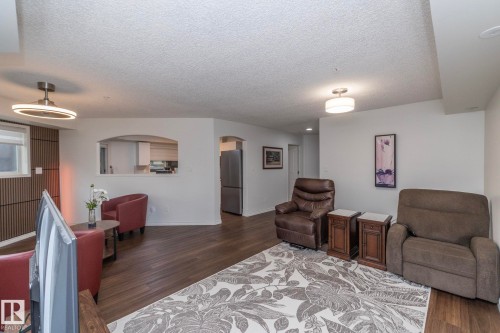 Spacious living area featuring wood-finish flooring, white walls, and a decorative slatted accent wall - 111 182 Haddow Close, Edmonton, AB 