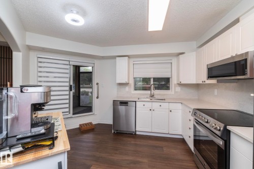 Modern kitchen featuring wood-finish flooring, white cabinetry, light-toned countertops, and stainless steel appliances including a range, dishwasher, and microwave - 111 182 Haddow Close, Edmonton, AB 