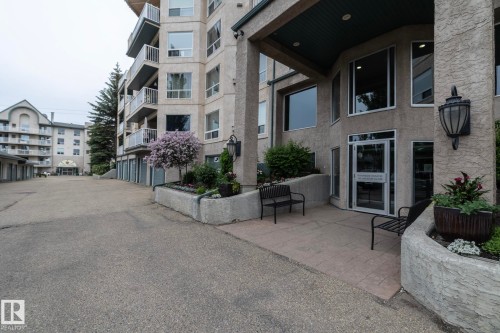 Building exterior featuring a stucco finish, multiple balconies with white railings, and a prominent entrance with large windows - 111 182 Haddow Close, Edmonton, AB 