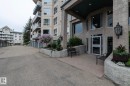 Building exterior featuring a stucco finish, multiple balconies with white railings, and a prominent entrance with large windows - 111 182 Haddow Close, Edmonton, AB 