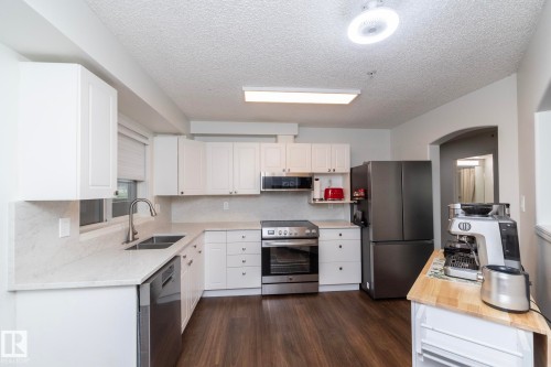 Modern kitchen featuring white shaker cabinetry, light-toned countertops with integrated backsplash, and wood-finish flooring - 111 182 Haddow Close, Edmonton, AB 