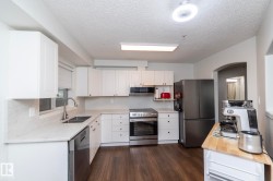 Modern kitchen featuring white shaker cabinetry, light-toned countertops with integrated backsplash, and wood-finish flooring - 