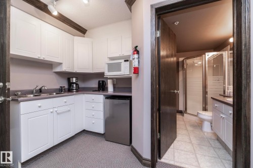 Compact kitchenette featuring white cabinetry, a stainless steel sink, and a built-in microwave - 111 182 Haddow Close, Edmonton, AB 