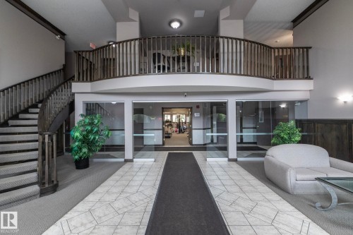 Multi-level lobby featuring a grand staircase with dark wood-finish railings, an upper-level balcony, and a tiled entryway - 111 182 Haddow Close, Edmonton, AB 