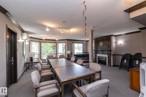 Spacious room featuring a large table with seating, multiple windows, a decorative fireplace, track lighting, and carpet flooring - 111 182 Haddow Close, Edmonton, AB 