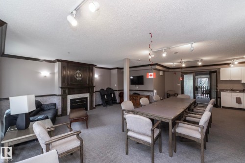 Spacious common area featuring a dark wood mantel fireplace with a light-colored surround, track lighting, wall sconces, and carpet flooring - 111 182 Haddow Close, Edmonton, AB 