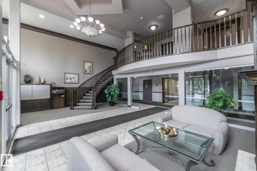 Two-story lobby featuring a grand staircase with dark wood railing, ceramic tile flooring, a chandelier, and a second-story overlook - 111 182 Haddow Close, Edmonton, AB 
