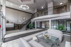 Two-story lobby featuring a grand staircase with dark wood railing, ceramic tile flooring, a chandelier, and a second-story overlook - 