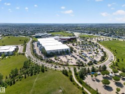 Expansive commercial property featuring multiple large buildings with light-colored roofing, extensive paved parking areas, and surrounding green spaces - 