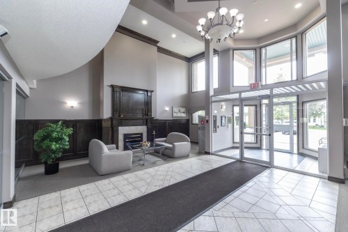Lobby entrance featuring large windows, a grand chandelier, and a fireplace with a dark wood surround - 111 182 Haddow Close, Edmonton, AB 