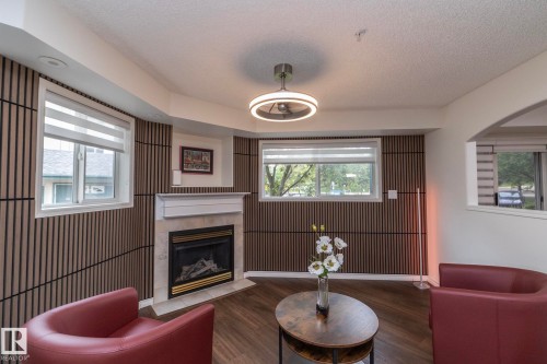 Living area featuring a gas fireplace with a stone surround and mantle, wood-finish flooring, and slatted accent walls - 111 182 Haddow Close, Edmonton, AB 