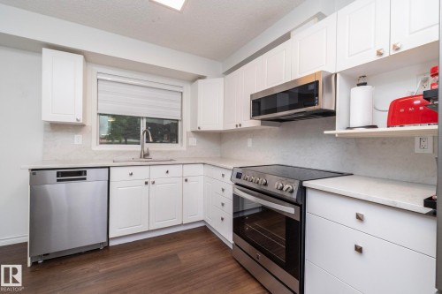 Modern kitchen featuring white cabinetry, light-toned countertops, and a full suite of stainless steel appliances including an electric range and microwave - 111 182 Haddow Close, Edmonton, AB 