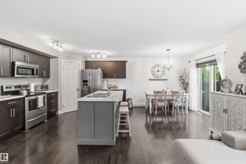 Open-concept kitchen and dining area featuring dark wood-finish flooring, a kitchen island with seating, stainless steel appliances, and a sliding glass door to the exterior - 20013 131 Avenue, Edmonton, AB 