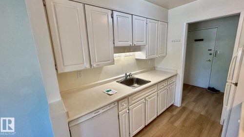 Kitchen featuring white cabinetry, light-toned countertops, a stainless steel sink, a built-in dishwasher, and wood-finish flooring - 203 11445 41 Avenue, Edmonton, AB 