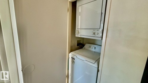 Dedicated laundry closet featuring a white stacked washer and dryer unit - 203 11445 41 Avenue, Edmonton, AB 