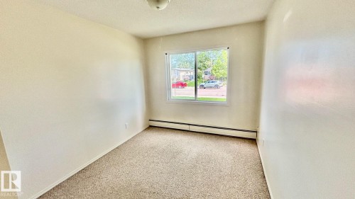 Carpeted interior space featuring a double-paned window, baseboard heating unit, and a ceiling-mounted light fixture - 203 11445 41 Avenue, Edmonton, AB 