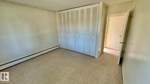Spacious room featuring neutral carpeting and a full wall of bi-fold louvered closet doors - 203 11445 41 Avenue, Edmonton, AB 