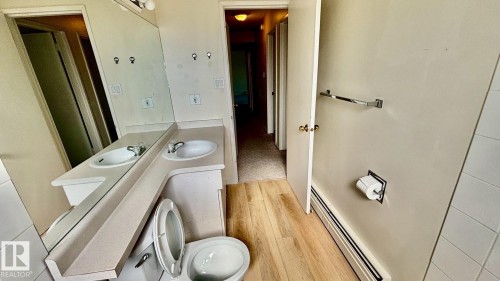 Vanity area featuring dual integrated sinks with chrome faucets, a wall-mounted mirror, and wood-finish flooring - 203 11445 41 Avenue, Edmonton, AB 