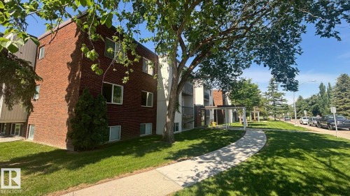 Brick exterior building with multiple windows, surrounded by manicured green lawns and mature trees - 203 11445 41 Avenue, Edmonton, AB 