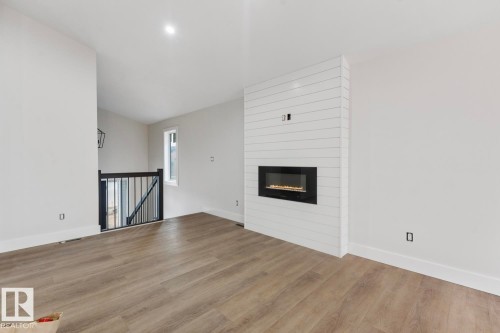 Living area featuring a modern linear fireplace with a shiplap surround, wood-finish flooring, recessed lighting, and a window providing natural light - 301 Fundy Way, Cold Lake, AB - Indoor With Fireplace