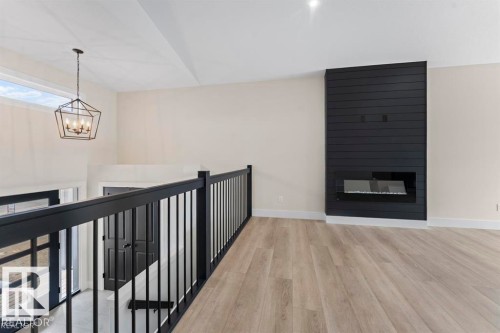 Open-concept living space with light wood-finish flooring, a contemporary black shiplap feature wall with an electric fireplace, and a striking black geometric chandelier - 301 Fundy Way, Cold Lake, AB - Indoor With Fireplace