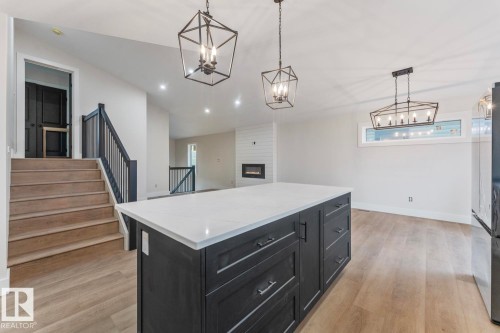 Spacious open-concept interior featuring a substantial kitchen island with a light-toned countertop, wood-finish flooring, recessed lighting, and modern geometric pendant fixtures - 301 Fundy Way, Cold Lake, AB - Indoor