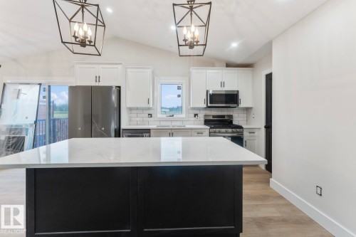 Kitchen featuring a large central island with a light-toned countertop, white cabinetry, stainless steel appliances, and wood-finish flooring - 301 Fundy Way, Cold Lake, AB - Indoor Photo Showing Kitchen With Upgraded Kitchen
