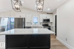 Kitchen featuring a large central island with a light-toned countertop, white cabinetry, stainless steel appliances, and wood-finish flooring - 