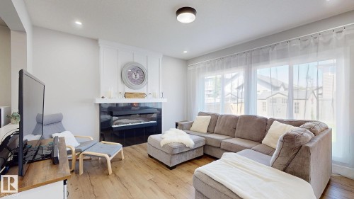 Living area featuring wood-finish flooring, a contemporary electric fireplace with a dark tile surround and white mantel, and large windows providing ample natural light - 312 West Haven Drive, Leduc, AB 