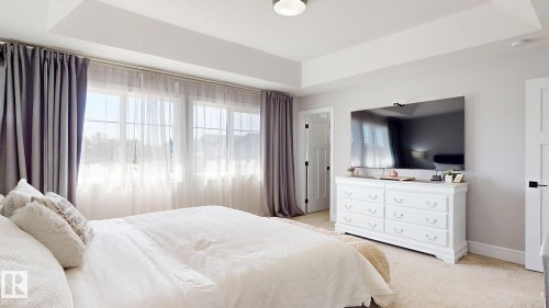 Tray ceiling bedroom featuring multiple windows with sheer and blackout drapery, light neutral wall color, and carpet flooring - 312 West Haven Drive, Leduc, AB 