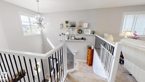 Staircase featuring dark spindle railings, a contemporary chandelier, and a window providing natural illumination - 312 West Haven Drive, Leduc, AB 