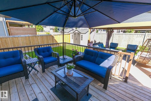 Outdoor wooden deck with black metal railings, featuring a blue umbrella and a pergola structure - 312 West Haven Drive, Leduc, AB 