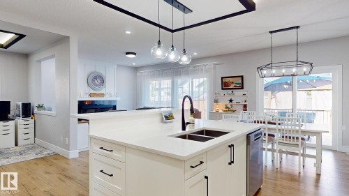 Kitchen island featuring a dual-basin sink with a matte black faucet, integrated dishwasher, and white cabinetry with black hardware - 312 West Haven Drive, Leduc, AB 