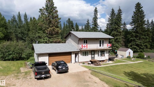Two-story residence with light-toned siding, attached garage featuring a wood-finish door, and a second-story balcony - 58403 Rr 60, Rural Barrhead County, AB - Outdoor