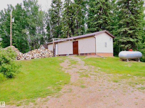 Utility building featuring light-colored siding and a brown roof, surrounded by mature trees - 58403 Rr 60, Rural Barrhead County, AB - Outdoor