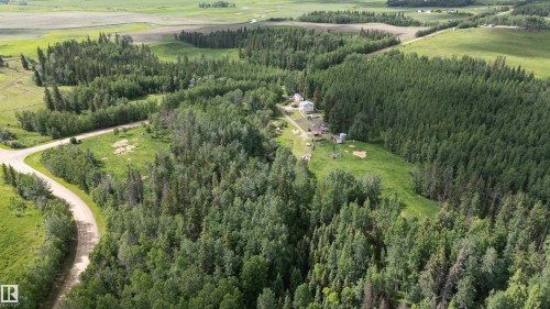 Extensive acreage featuring diverse tree coverage, open grassy areas, multiple structures, and a winding gravel road - 58403 Rr 60, Rural Barrhead County, AB - Outdoor With View