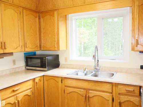 Kitchen featuring natural wood cabinetry, light-toned countertops, a double basin stainless steel sink with a high-arc pull-down faucet, and a large window overlooking natural scenery - 58403 Rr 60, Rural Barrhead County, AB - Indoor Photo Showing Kitchen With Double Sink