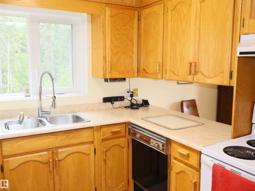 Kitchen featuring ample wood cabinetry, a double basin stainless steel sink with a high-arc faucet, light-toned countertops, and a built-in electric cooktop - 58403 Rr 60, Rural Barrhead County, AB - Indoor Photo Showing Kitchen With Double Sink