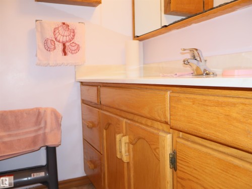 Wood-finish vanity with panel doors and drawers, topped with a light-colored countertop featuring an integrated sink and chrome faucet - 58403 Rr 60, Rural Barrhead County, AB - Indoor