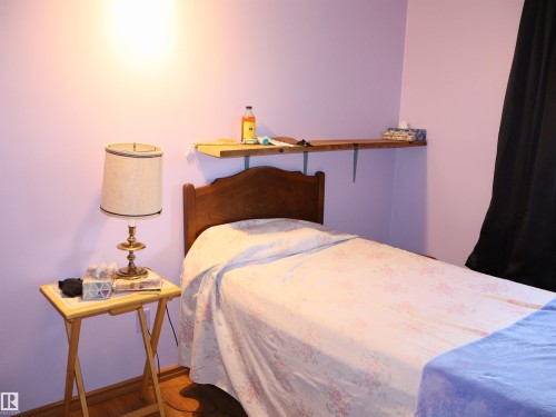 Wood-finish flooring with light-toned baseboards, soft purple wall paint, and a built-in wood shelf with decorative brackets - 58403 Rr 60, Rural Barrhead County, AB - Indoor Photo Showing Bedroom