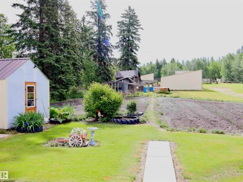 Expansive property featuring a vibrant green lawn, a greenhouse with a metal roof and wooden door, a concrete pathway, a tilled garden area, and mature trees - 58403 Rr 60, Rural Barrhead County, AB - Outdoor