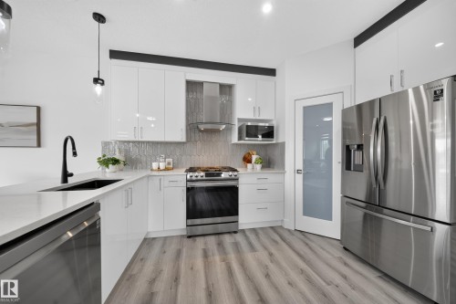 Modern kitchen featuring white glossy cabinetry, stainless steel appliances, a matte black faucet, light wood-finish flooring, and a patterned tile backsplash - 1099 Eaton Road, Edmonton, AB 