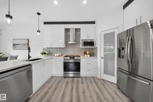 Modern kitchen featuring white cabinetry, stainless steel appliances, a white countertop, and wood-finish flooring - 1099 Eaton Road, Edmonton, AB 