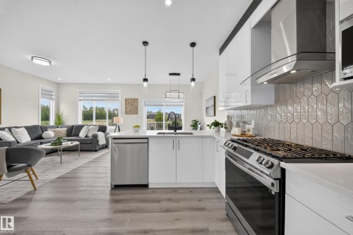 Modern kitchen featuring white cabinetry, quartz countertops, stainless steel appliances, and a unique elongated hexagonal tile backsplash - 1099 Eaton Road, Edmonton, AB 