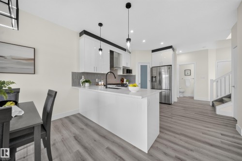 Modern kitchen featuring a central island with a light-toned countertop, sleek white cabinetry, and a dark tile backsplash - 1099 Eaton Road, Edmonton, AB 