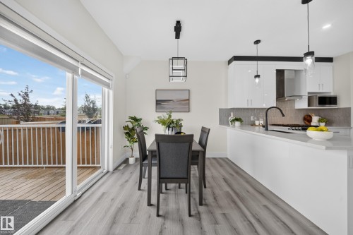Open-concept dining and kitchen area featuring light wood-finish flooring, white cabinetry, a kitchen island with a light countertop, and a sliding glass door to an outdoor deck - 1099 Eaton Road, Edmonton, AB 