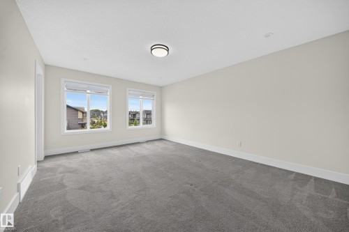 Spacious room featuring neutral painted walls, gray patterned carpet, and multiple windows with white trim - 1099 Eaton Road, Edmonton, AB 