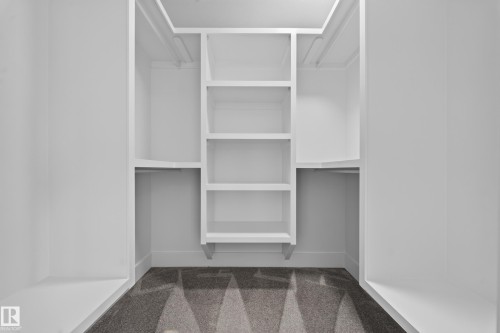 Custom built-in closet system featuring white shelving, multiple hanging rods, and a patterned grey carpet - 1099 Eaton Road, Edmonton, AB 
