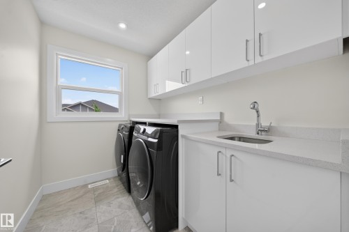 Laundry room featuring white cabinetry, light-colored countertops, a stainless steel sink with a pull-down faucet, and tiled flooring - 1099 Eaton Road, Edmonton, AB 