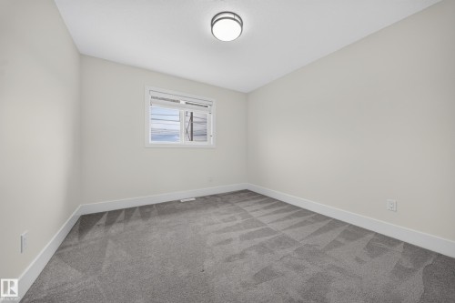 Neutral-toned interior room featuring light gray walls, patterned gray carpet, white trim, and a flush mount ceiling light fixture - 1099 Eaton Road, Edmonton, AB 